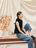 Woman sitting relaxed in black sleeveless velvet mandarin collar qipao style blouse, paired with jeans