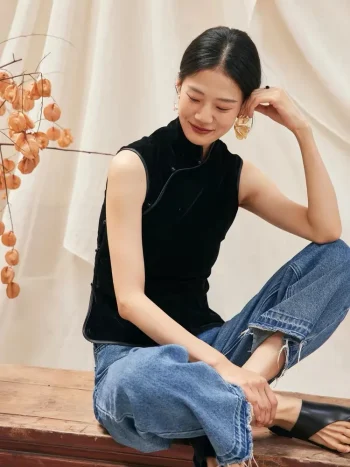 Woman sitting on bench in black sleeveless velvet mandarin collar qipao style blouse, casual elegant look