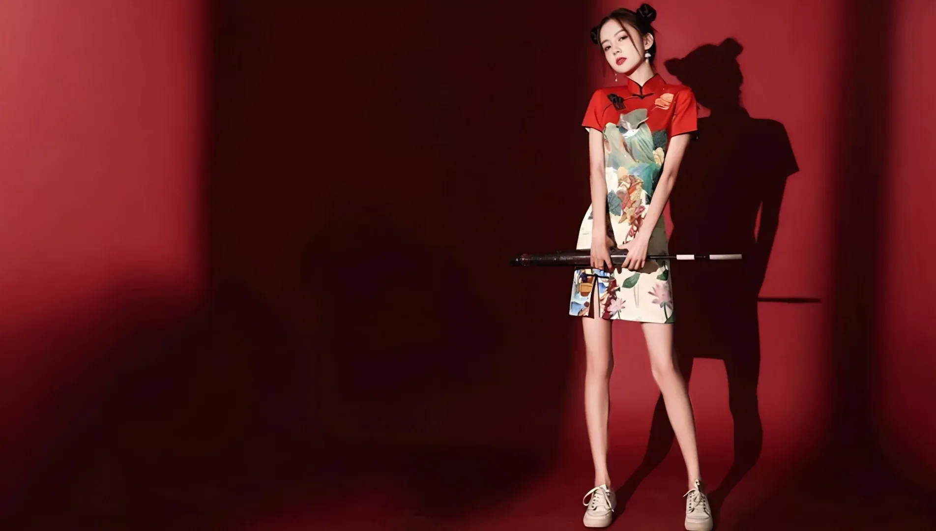 Young woman in modern improved short cheongsam with double bun hairstyle, new chinese style fashion studio shot on red background