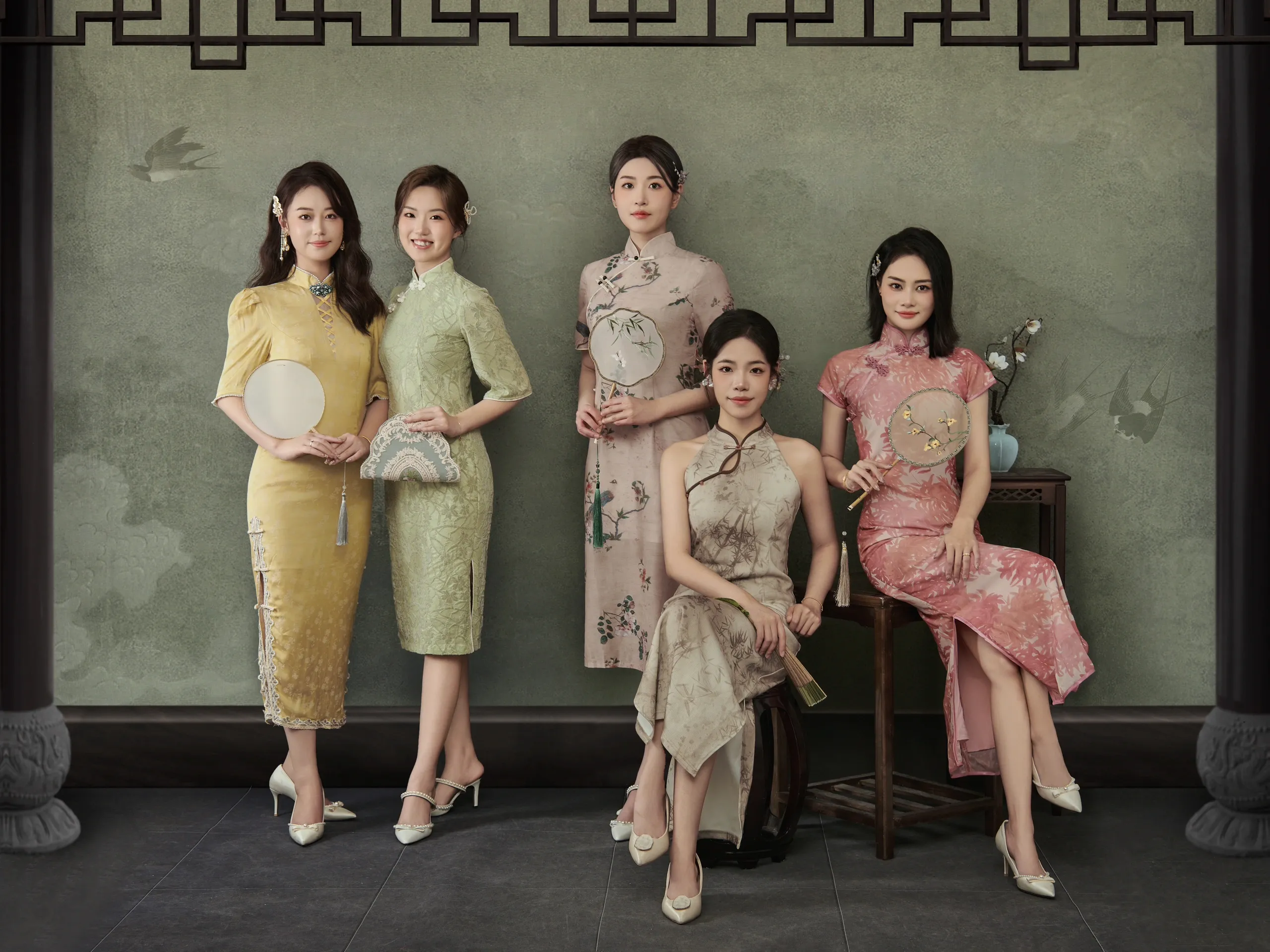 Group of women wearing elegant modern qipao cheongsam dresses in soft green tones, showcasing diverse styles of traditional Chinese qipao dress—including floral prints and solid colors with fans—perfect for those exploring what a qipao or cheongsam dress is.