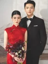 Elegant couple standing wedding portrait, bride in red long satin wedding cheongsam (qipao) holding bridal bouquet, traditional chinese wedding dress with mountain background