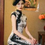 Elegant woman sitting in a vintage studio, wearing 1920s Shanghai Chinese silk cheongsam with ink-wash bamboo print, black lace trim, and high slit, showcasing retro glamour.