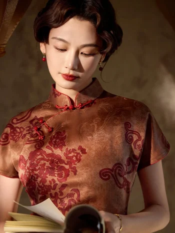 Close-up shot of a woman in a 1930s reddish-brown floral silk qipao, reading a book while highlighting the intricate red floral print, traditional mandarin collar, and handcrafted knot buttons on the placket.
