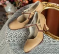 Pair of 1920s vintage beige genuine leather qipao Mary Janes with brown contrast trim, displayed on delicate lace fabric against an ornate golden mirror background.