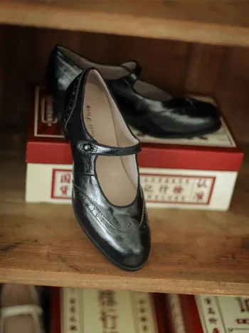 Black Margarita 1920s Vintage Schoolgirl Style Leather Qipao Shoes, close-up shot showcasing the brogue stitching and leather texture, displayed on a wooden shelf with vintage Chinese-style shoe boxes.