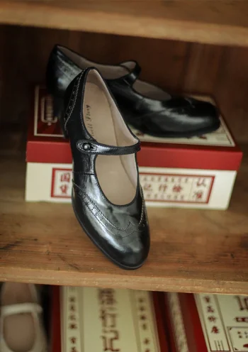 Black Margarita 1920s Vintage Schoolgirl Style Leather Qipao Shoes, close-up shot showcasing the brogue stitching and leather texture, displayed on a wooden shelf with vintage Chinese-style shoe boxes.