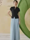 Model wearing a black modern qipao inspired top, a sleek black chinese mandarin collar qipao top with short sleeves, styled with light blue wide leg trousers in a soft studio setting.
