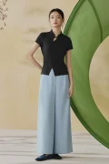 Model wearing a black modern qipao inspired top, a sleek black chinese mandarin collar qipao top with short sleeves, styled with light blue wide leg trousers in a soft studio setting.