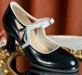 Close-up of 1920s vintage black patent leather qipao Mary Jane shoes with crisp white contrast trim, showcasing the glossy leather finish and geometric cutout details on an ornate mirror.