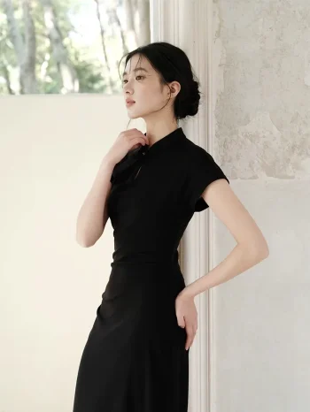 Profile shot of a woman in a black qipao dress, leaning against a textured wall. The women qipao’s fitted cut and cap sleeves highlight its modern take on traditional Chinese fashion.