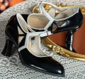 Close-up of 1920s vintage black genuine leather qipao Mary Janes with white contrast trim and geometric cutouts, placed on delicate lace fabric.
