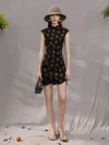 Full-body shot of a model in a black sleeveless short qipao dress with rose print, paired with a sun hat and holding a handbag in a neutral studio setting.
