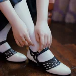 Black and white 1920s Qipao dress goat leather shoes with classic hollow out details, worn with white socks, a model adjusts the shoes on wooden floor, ideal for vintage cheongsam styling.