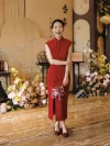 Cheongsam for Wedding - Bride in modern red silk cheongsam holding calla lilies at a traditional Chinese wedding, wearing elegant form-fitting sleeveless qipao with mandarin collar, standing in front of wedding backdrop with floral arrangements.