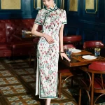 Model wearing a Chinese silk white floral print qipao dress with green trim, standing in a vintage restaurant to show the elegant silhouette and smooth silk texture.