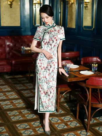 Model wearing a Chinese silk white floral print qipao dress with green trim, standing in a vintage restaurant to show the elegant silhouette and smooth silk texture.