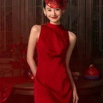 A bride poses in a bold red wedding cheongsam dress, paired with a traditional red paper cut headpiece that echoes Chinese wedding traditions. This elegant cheongsam wedding dress features a fitted silhouette ideal for modern brides.