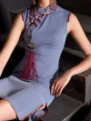 Close-up shot of a woman's misty blue short cheongsam dress, focusing on the traditional red frog buttons and pink tassel accessory of this women's cheongsams qipao.