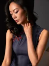 Close-up shot of a woman's neckline in a short sleeveless qipao dress, focusing on the traditional red frog buttons and fabric details of this women's qipao.