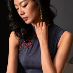 Close-up shot of a woman's neckline in a short sleeveless qipao dress, focusing on the traditional red frog buttons and fabric details of this women's qipao.