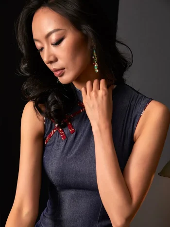 Close-up shot of a woman's neckline in a short sleeveless qipao dress, focusing on the traditional red frog buttons and fabric details of this women's qipao.