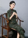 Model seated in a wooden chair wearing a custom green Momo qipao, showcasing the traditional frog buttons, 3/4 sleeves, and side slit design.