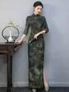 Model leaning on a traditional wooden table wearing a custom green qipao with plant print, showing the tailored fit and 3/4 sleeve design.