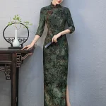 Model leaning on a traditional wooden table wearing a custom green qipao with plant print, showing the tailored fit and 3/4 sleeve design.