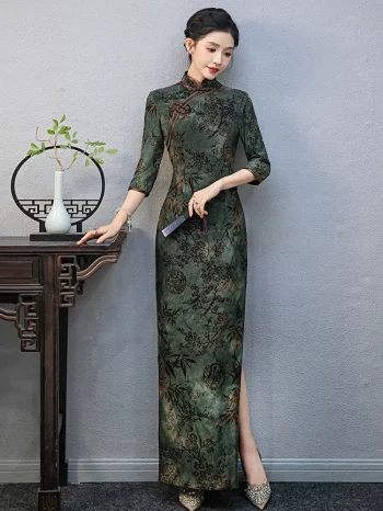 Model leaning on a traditional wooden table wearing a custom green qipao with plant print, showing the tailored fit and 3/4 sleeve design.