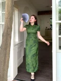 Plus size model wearing dark green floral print chinese qipao dress, elegant form-fitting cheongsam with traditional mandarin collar, posing with a folding fan in a bright doorway setting.