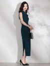Women's elegant dark green qipao (cheongsam) with high slit, rose jacquard fabric and red buttons, model in side view holding a black pearl handle handbag.