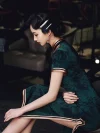 Side profile of a woman in dark green vintage floral qipao sitting, showcasing intricate floral patterns and satin trim in a classic interior.