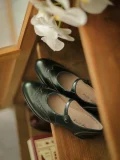 Emerald Green Margarita 1920s Vintage Schoolgirl Style Leather Qipao Mary Jane Shoes with brogue detailing, displayed on a vintage wooden shelf with white orchids for retro aesthetic.
