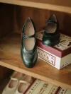 Rich emerald green Margarita 1920s vintage schoolgirl leather Qipao Mary Jane shoes with intricate brogue detailing, displayed on a vintage wooden shelf for nostalgic retro look.