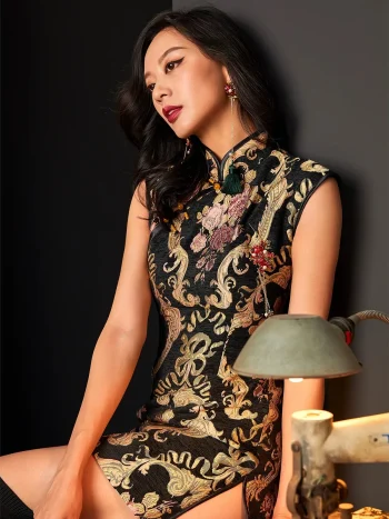 Elegant woman seated in a studio, wearing a fashion black and gold embroidered short qipao dress with intricate floral and baroque-style embroidery, showcasing the mandarin collar, tassel details, and luxurious texture of this black embroidered qipao.
