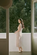 Back view of a woman standing on a balcony in a full-length cotton qipao dress, with side slits and midcentury Hong Kong retro styling for everyday elegance.