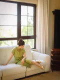 Shiny gold vintage genuine leather T strap high heel qipao sandals, worn with a retro green cheongsam on a white sofa by the window, showcasing elegant retro glamour under natural light