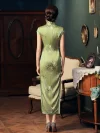 Back view of a woman in a green long cheongsam dress, standing in a vintage interior to show the dress's back zipper, full floral print pattern, and flowing hem.