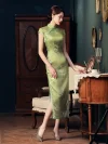 Full side view of a woman in a green cheongsam dress, standing by a wooden table in a vintage interior, highlighting the form-fitting silhouette, short sleeves, and high slit design.