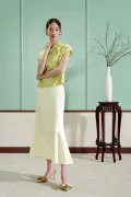 Full-body shot of a green modern cheongsam shirt, women's mulberry silk short sleeve qipao top with water drop collar, paired with a white mermaid skirt in a minimalist room.