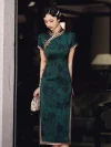 Full-length view of a woman in dark green vintage floral qipao, holding a delicate handbag to highlight the form-fitting cut and high collar.