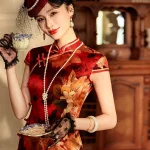 High-end women's mulberry silk cheongsam dress with red and yellow floral print, Old Shanghai vintage style. The model holds a teacup in a classic room, wearing a net hat and lace gloves, showcasing the elegant satin sheen of the silk fabric.