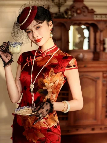 High-end women's mulberry silk cheongsam dress with red and yellow floral print, Old Shanghai vintage style. The model holds a teacup in a classic room, wearing a net hat and lace gloves, showcasing the elegant satin sheen of the silk fabric.