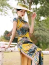 Model seated on a white birch fence, wearing a women high end yellow mulberry silk cheongsam dress with traditional Chinese landscape print, showcasing the elegant fit and satin sheen.