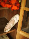 Ivory White Margarita 1920s Vintage Schoolgirl Style Leather Qipao Mary Jane Shoes, placed in a wooden cabinet with orange flowers, highlighting the classic brogue design for cheongsam outfits.