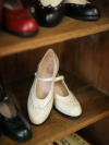 Ivory White Margarita 1920s Vintage Schoolgirl Style Leather Qipao Shoes with delicate brogue details, displayed on a vintage wooden shelf alongside other color options.