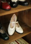 Ivory White Margarita 1920s Vintage Schoolgirl Style Leather Qipao Shoes with delicate brogue details, displayed on a vintage wooden shelf alongside other color options.