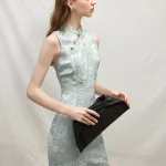 Elegant model holding a black clutch, wearing a light blue modern Chinese sleeveless short cheongsam dress, showcasing the delicate floral jacquard fabric and tailored silhouette.