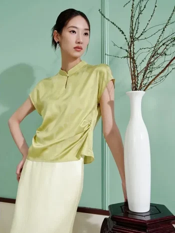 Side view of a woman wearing a light green mulberry silk modern cheongsam shirt, featuring a flattering ruched waist detail that enhances the silhouette of this elegant short sleeve qipao top.