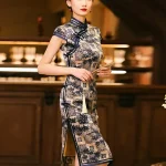 Elegant model wearing a misty blue bamboo pattern print brocade cheongsam dress, holding a traditional hand fan, standing in a vintage bar setting to showcase the dress's mandarin collar, frog buttons, and high slit.
